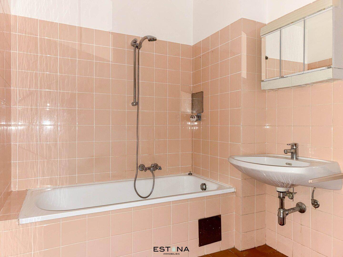 Badezimmer im 80er-Jahre-Stil mit rosa Fliesen, Badewanne, Duschvorrichtung und Waschbecken.