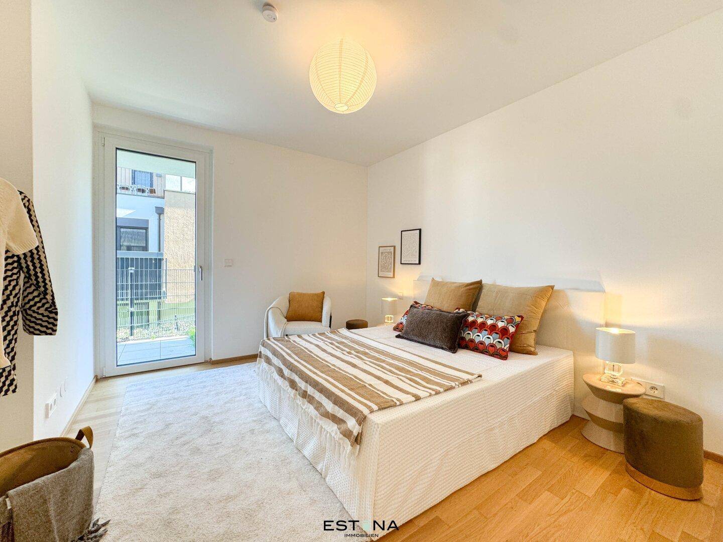 Helles Schlafzimmer mit Doppelbett, Teppich und großem Fenster, das viel Tageslicht hereinlässt.