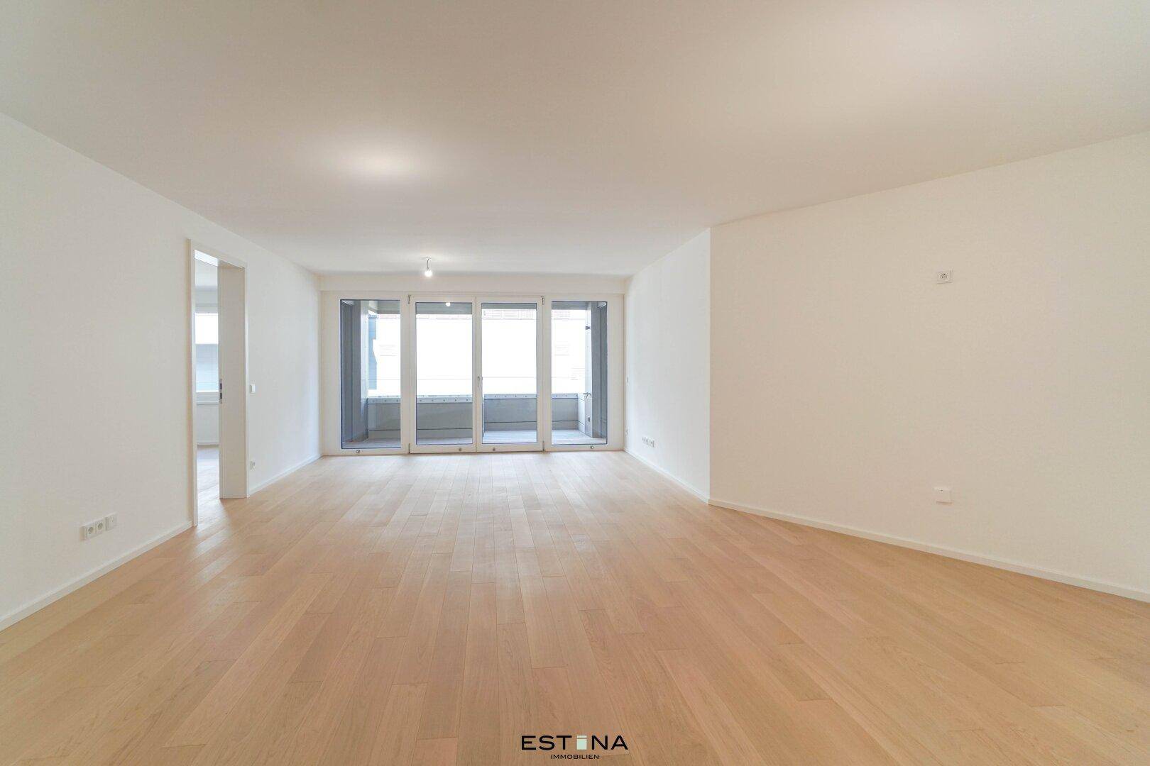 Heller, geräumiger Wohnbereich mit hellem Holzparkettboden und großen Schiebetüren zum Balkon.