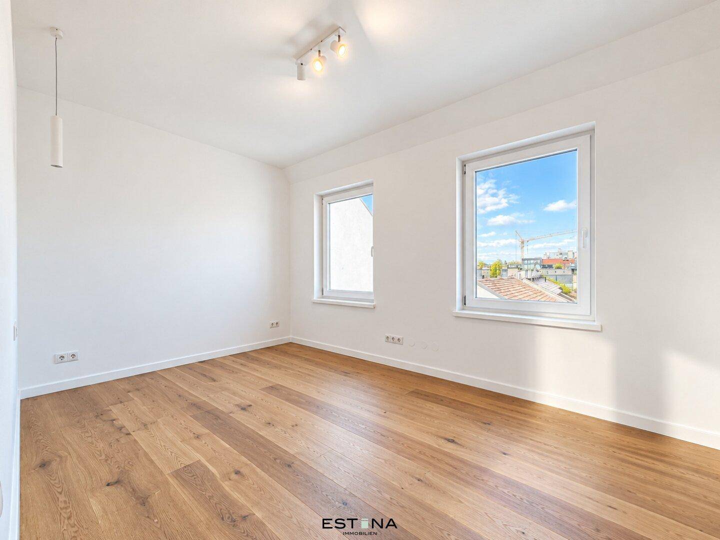 Heller Raum mit Holzboden und zwei Fenstern, die viel Tageslicht hereinlassen.