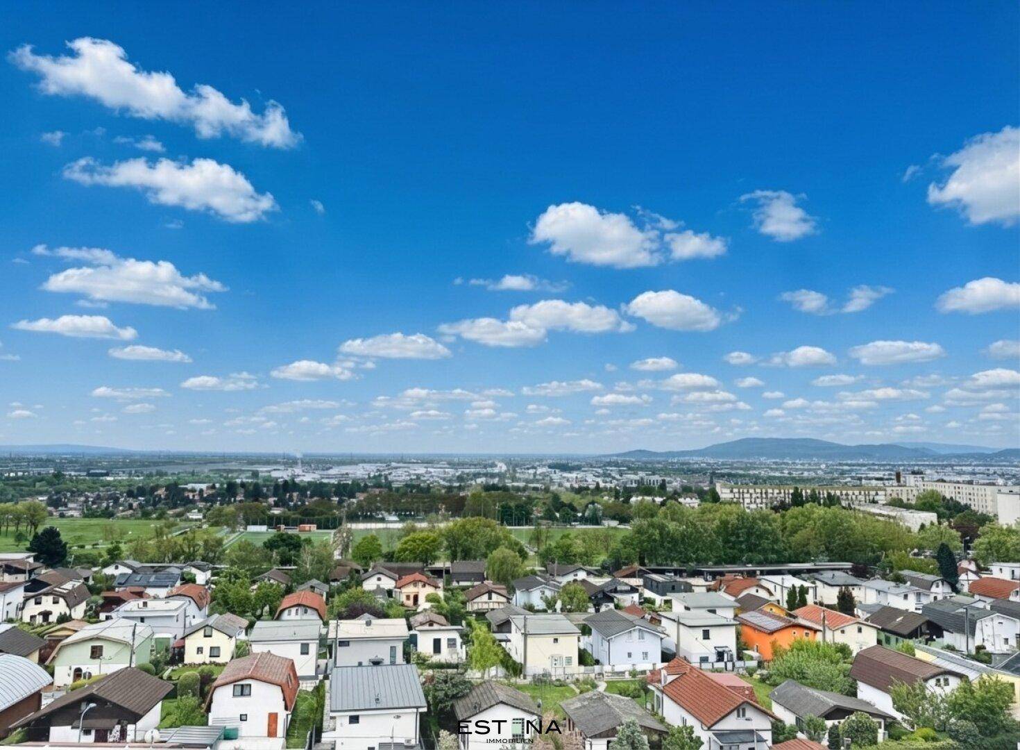 Panoramablick über eine weitläufige Wohnsiedlung mit viel Grün und einer malerischen Bergkulisse am Horizont.