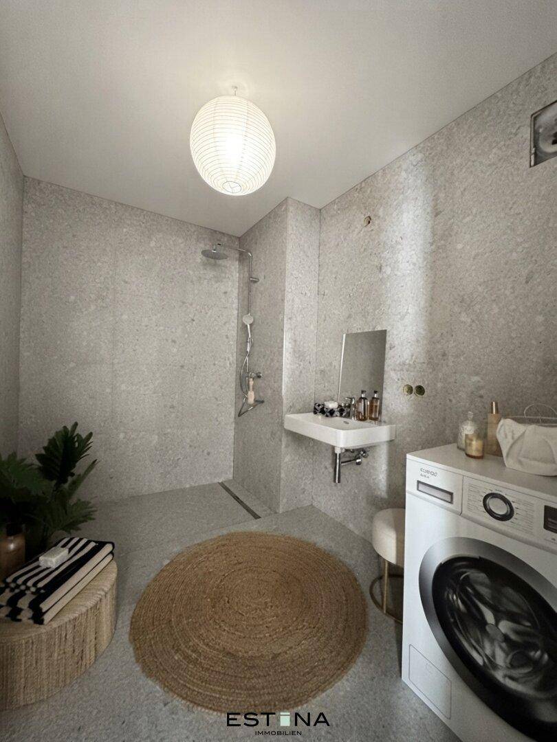 Modernes Badezimmer mit begehbarer Dusche, Waschmaschine und grauen Fliesen.