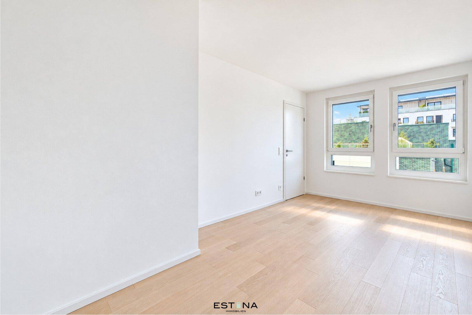 Freundliches Zimmer mit hellem Parkettboden und zwei Fenstern, die den Blick auf die Nachbarschaft freigeben.