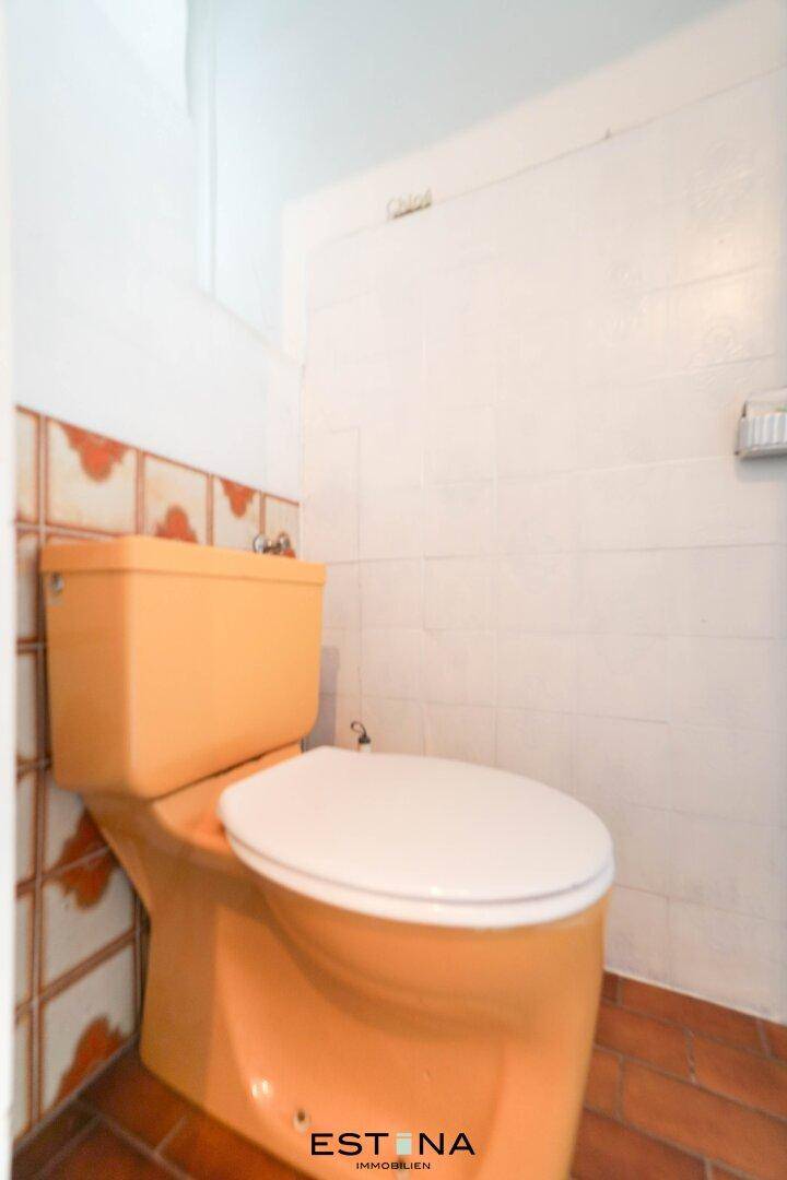 Separate Toilette mit orangefarbener Keramik und weißen Fliesen.