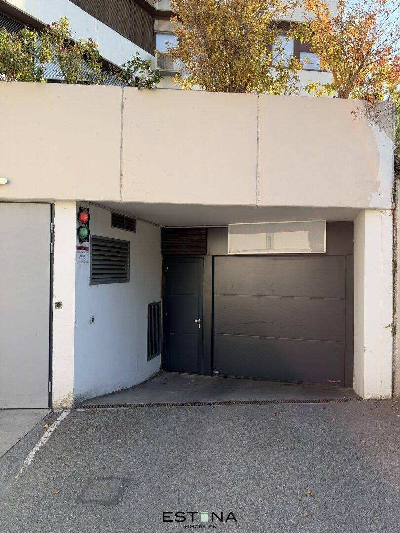 Eingangsbereich einer Tiefgarage mit schwarzem Garagentor und Ampelsystem für die Zufahrt.