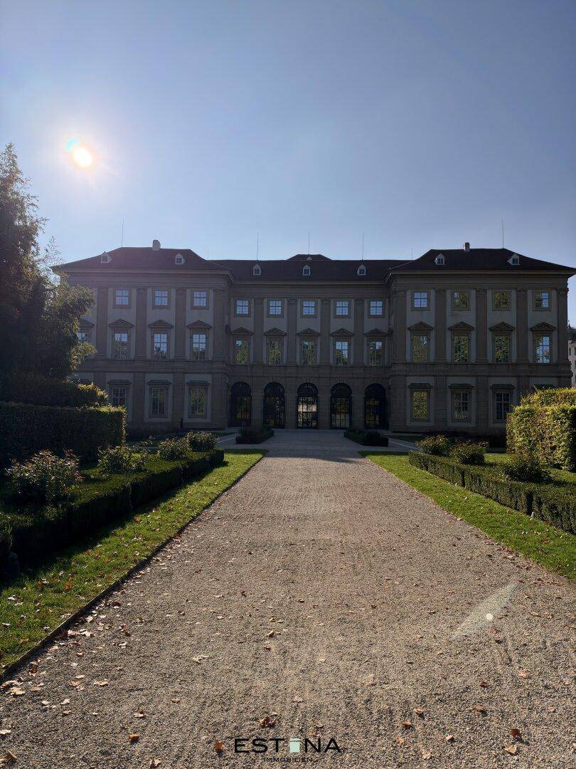 Prächtiges historisches Gebäude mit weitläufigem Garten und gepflegten Grünflächen unter strahlendem Sonnenschein.