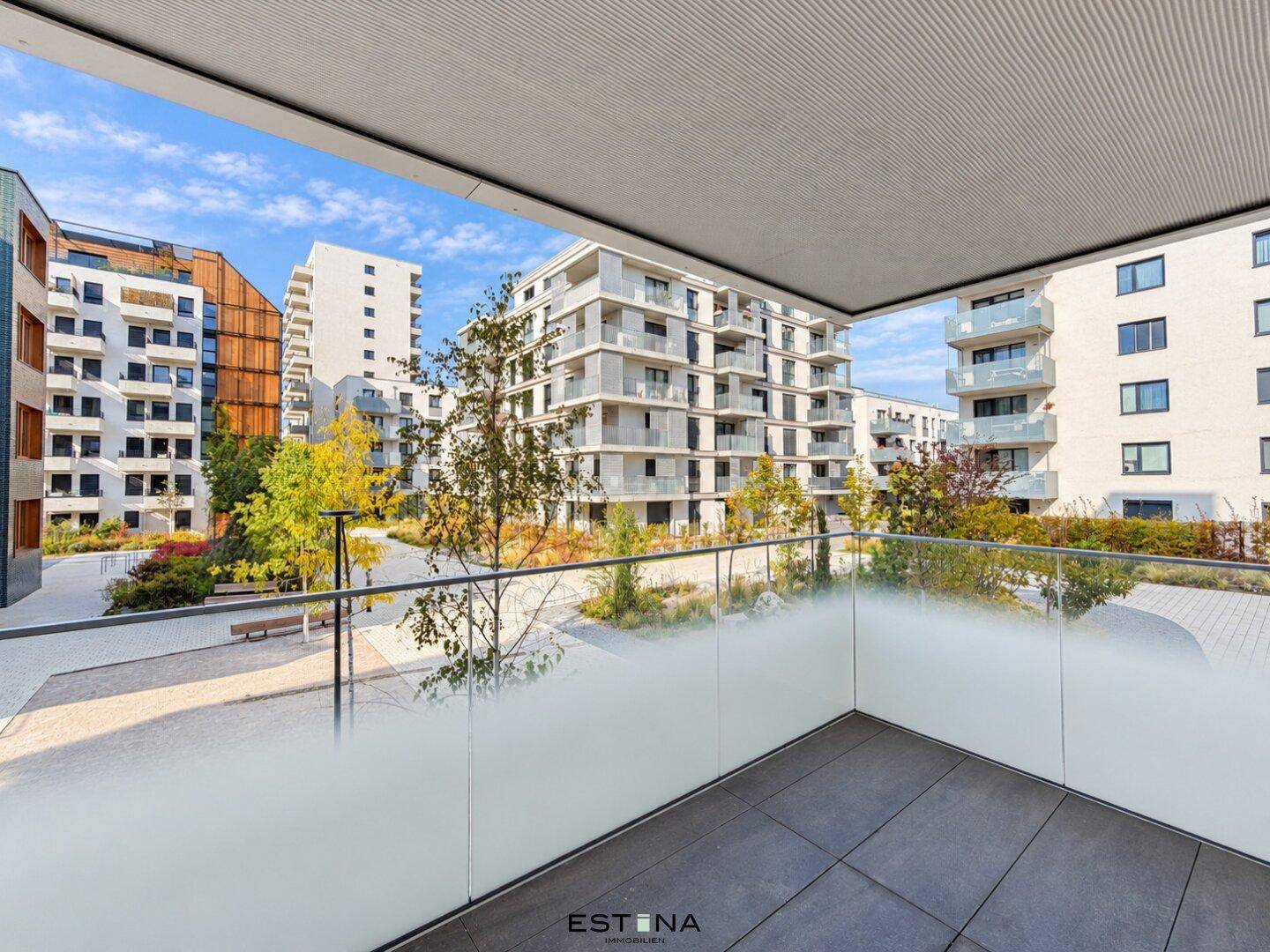 Blick von einem modernen Balkon mit Milchglasgeländer auf eine Wohnanlage mit Grünflächen.
