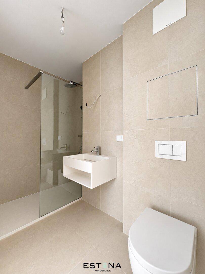 Modernes Badezimmer mit beigefarbenen Fliesen, schwebendem Waschtisch und begehbarer Dusche.