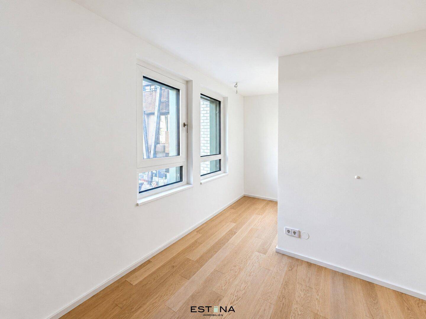 Helles, leeres Zimmer mit Parkettboden und zwei Fenstern, ideal als Schlaf- oder Arbeitszimmer.