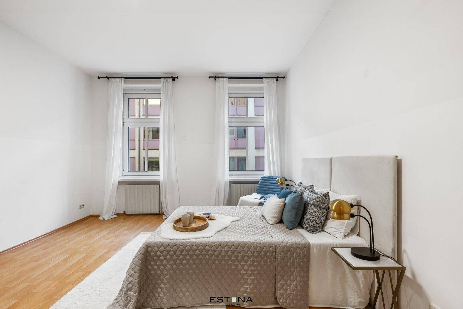 Helles Schlafzimmer mit Doppelbett, Nachttischen und viel Tageslicht durch die Fenster.