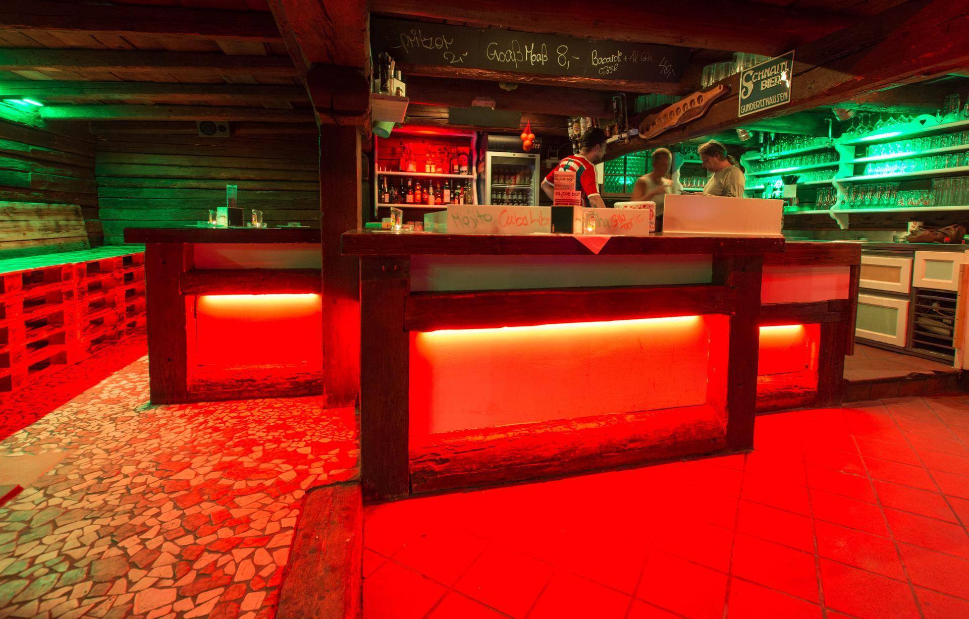 Hauptbarbereich mit roter Beleuchtung, gefliestem Boden und Regalen voller Gläser.