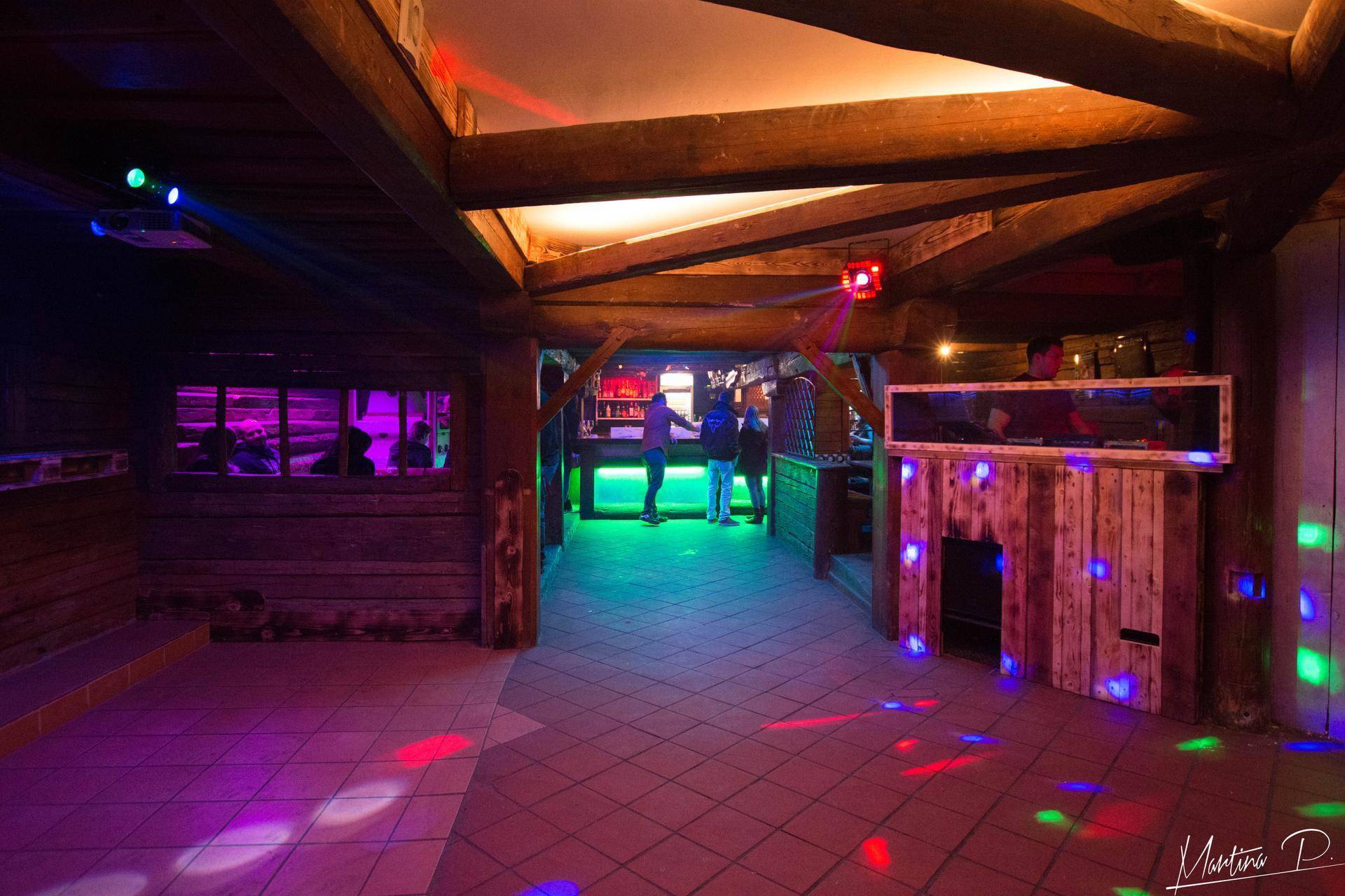 Geräumiger Barbereich mit Holzbalken, Fliesenboden und farbiger Disco-Beleuchtung.