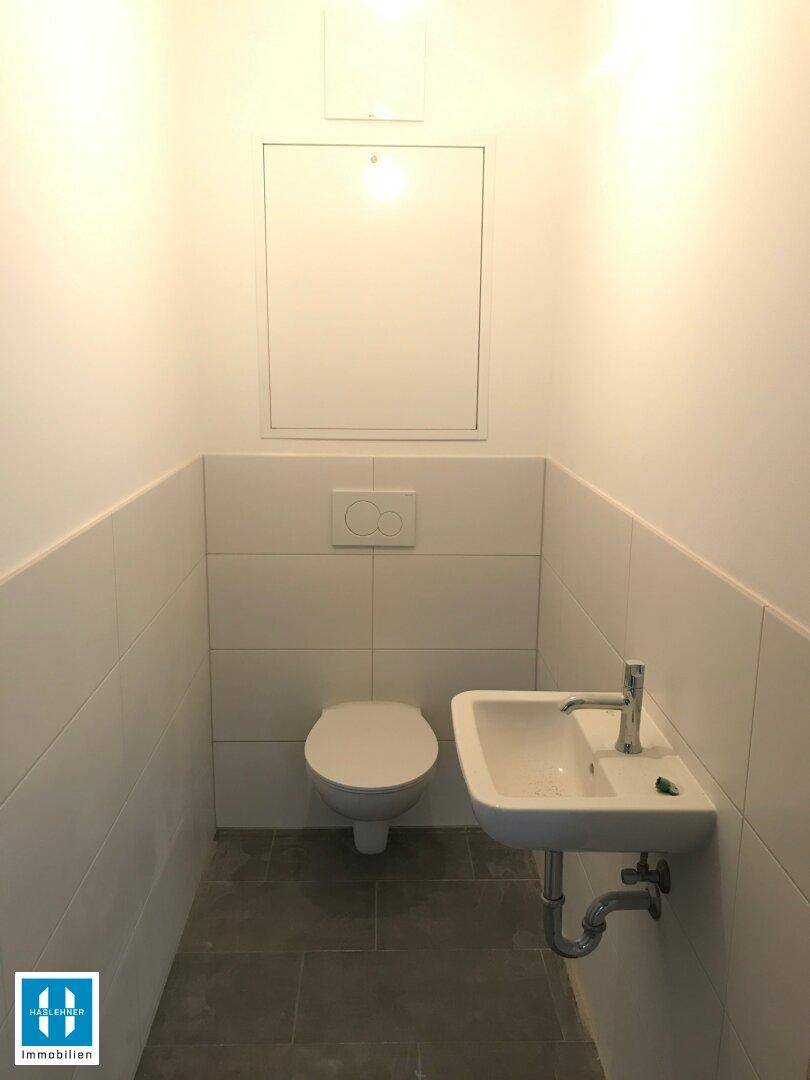 Modernes Gäste-WC mit wandhängendem WC, kleinem Waschbecken und Fliesenboden in hellem Design.