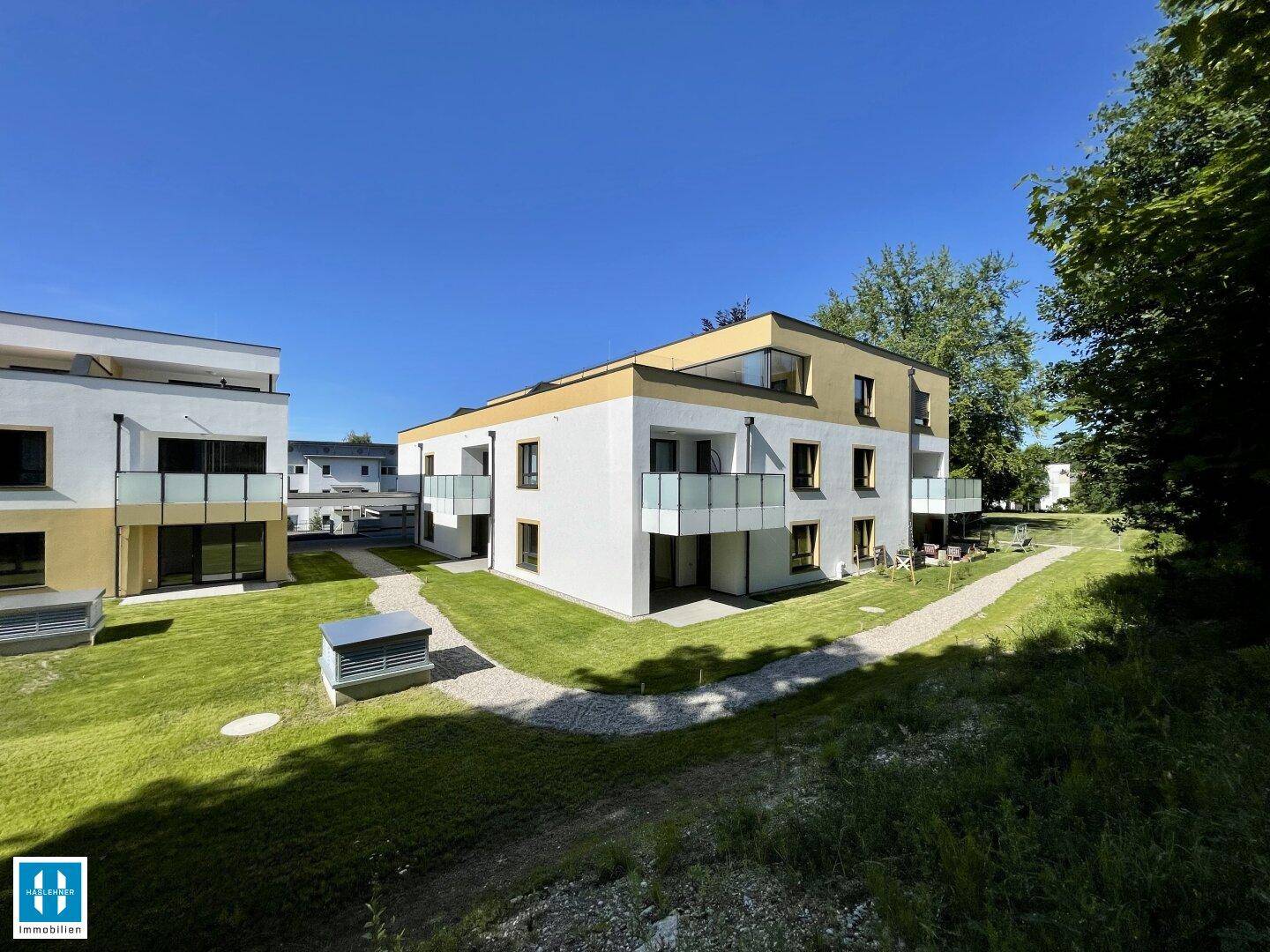 Neubauwohnungen mit Balkonen und einer Mischung aus weißer und gelber Fassade, eingebettet in eine grüne Umgebung.