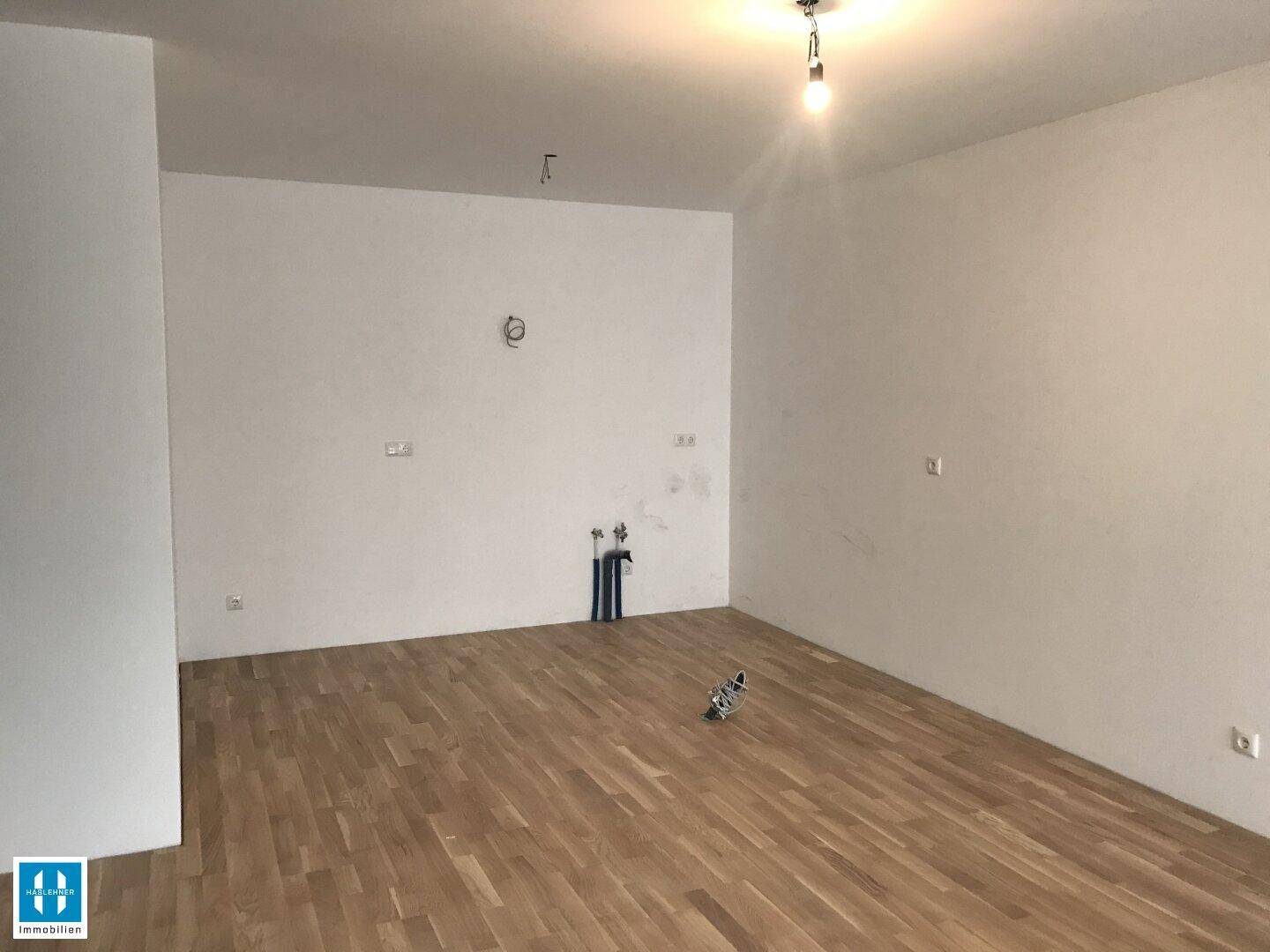 Leerer Raum mit Holzboden und sichtbaren Anschlüssen für eine zukünftige Küche.
