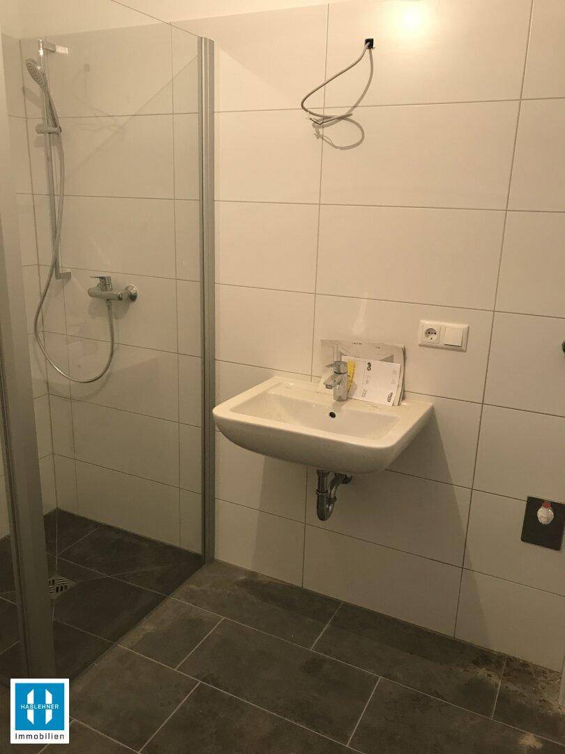 Helles Badezimmer mit Duschkabine und Waschbecken, ausgestattet mit weißen Wandfliesen.