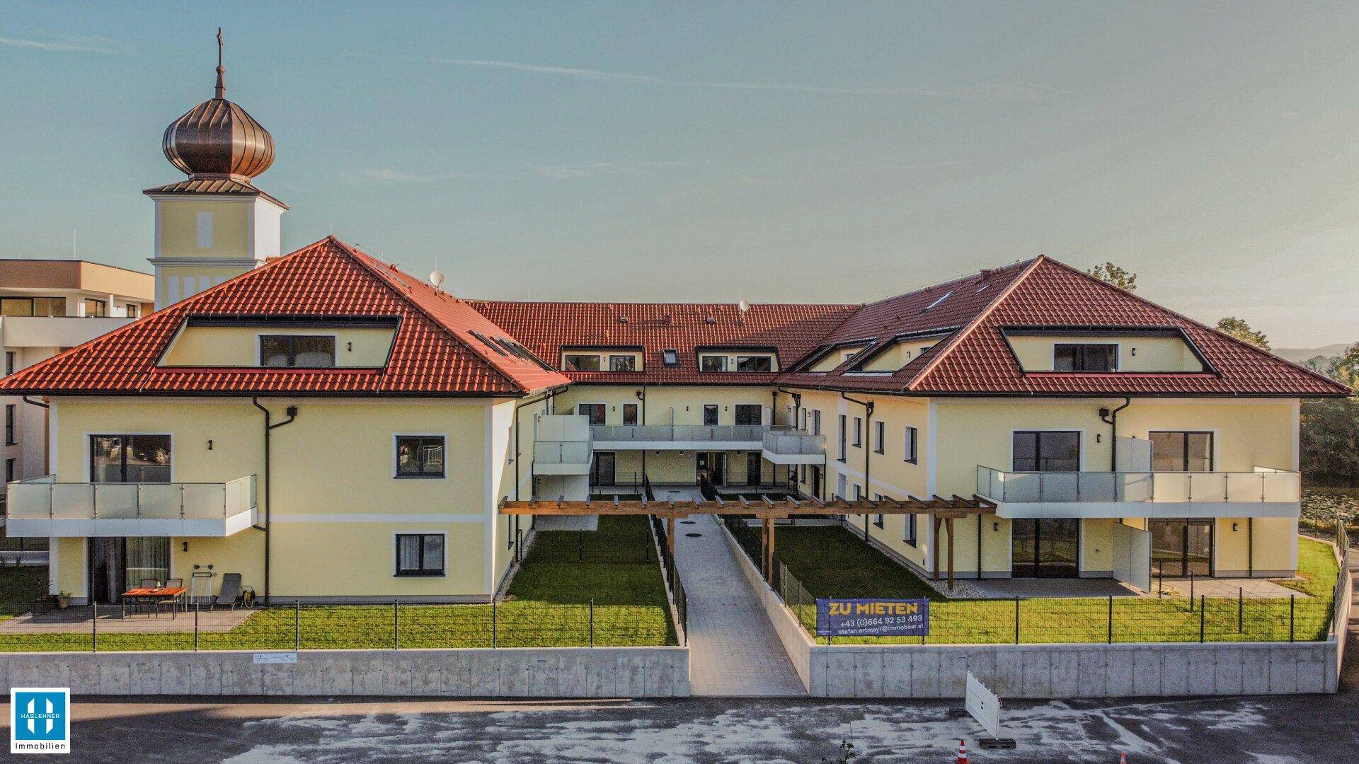 Attraktives Mehrfamilienhaus mit Balkonen, rotem Ziegeldach und einem markanten Turm.