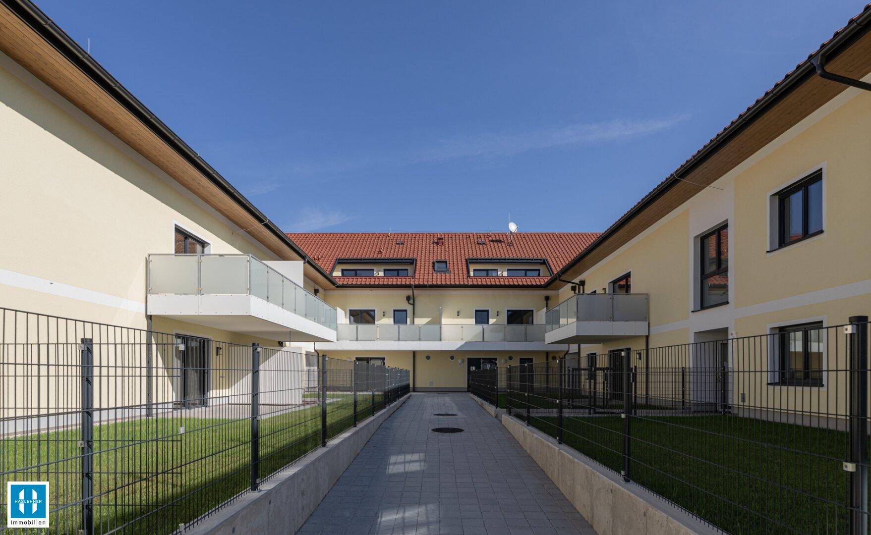 Innenhof des Wohnkomplexes mit gepflegten Rasenflächen, Balkonen und einem zentralen Weg.
