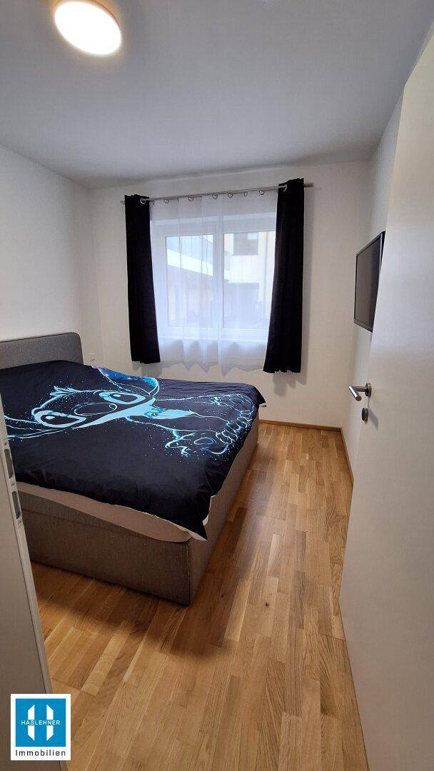 Gemütliches Schlafzimmer mit Holzboden, Doppelbett und Fenster mit dunklen Vorhängen.