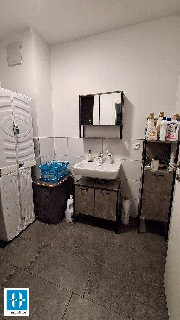 Funktionaler Waschraum mit Waschmaschine, Waschbecken und Spiegelschrank.