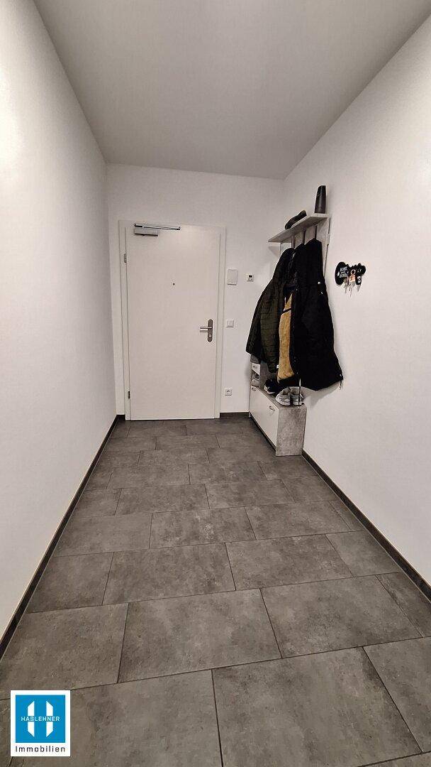 Heller Flur mit modernen Fliesen und Garderobe, die zum Eingangsbereich führt.