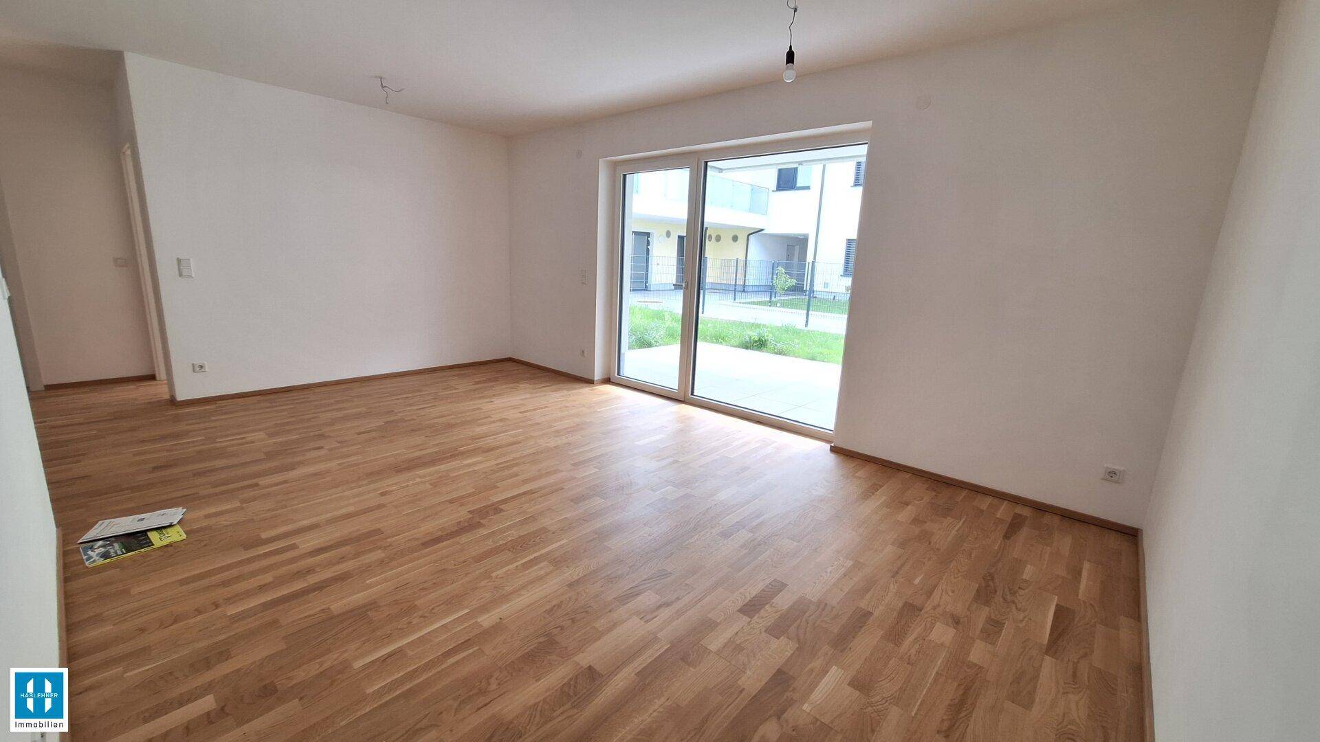 Heller, leerer Wohnraum mit Holzboden und großer Schiebetür, die ins Freie führt.