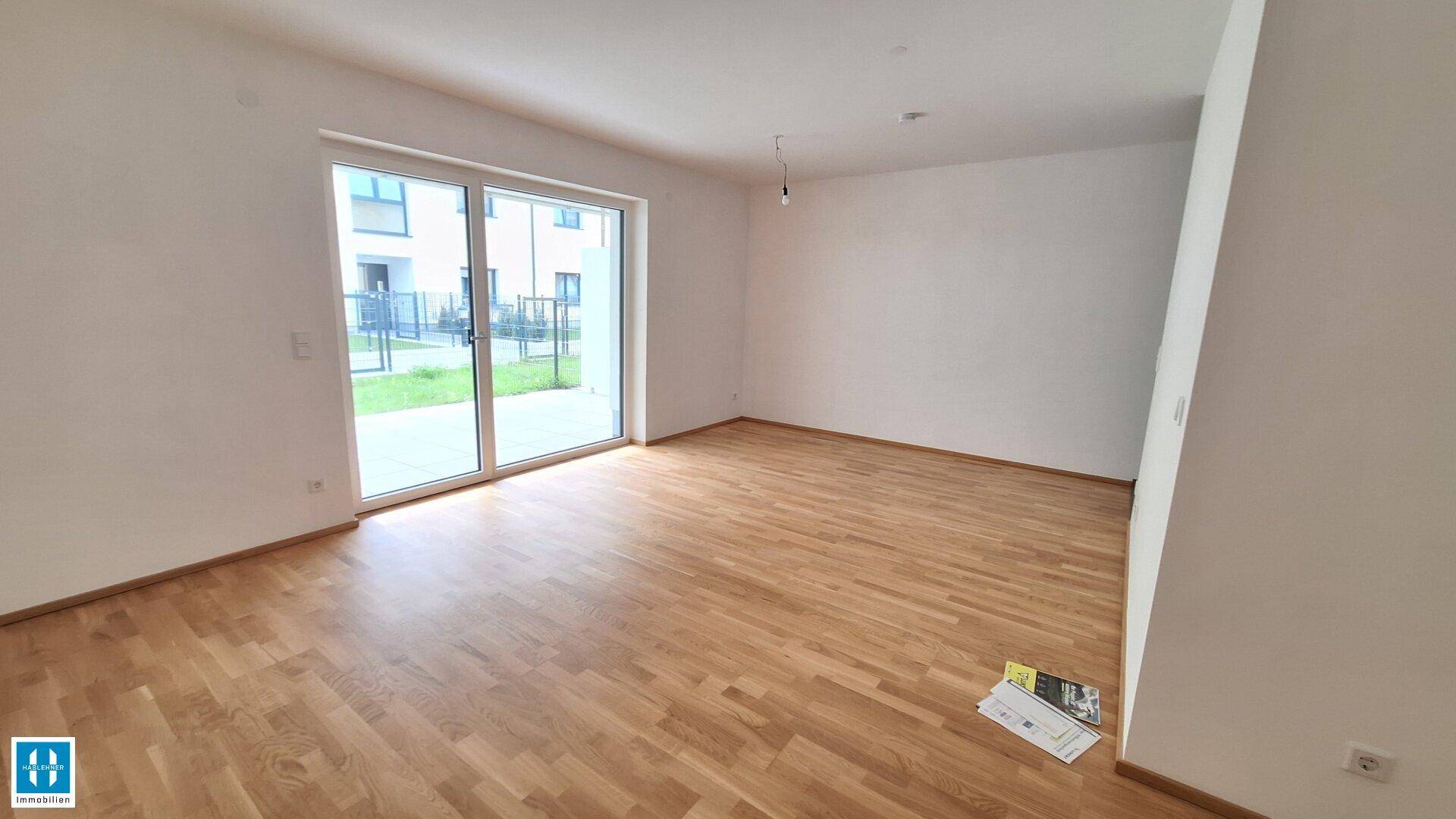 Geräumiger, unmöblierter Wohnbereich mit Holzboden und Zugang zu einer Außenterrasse.