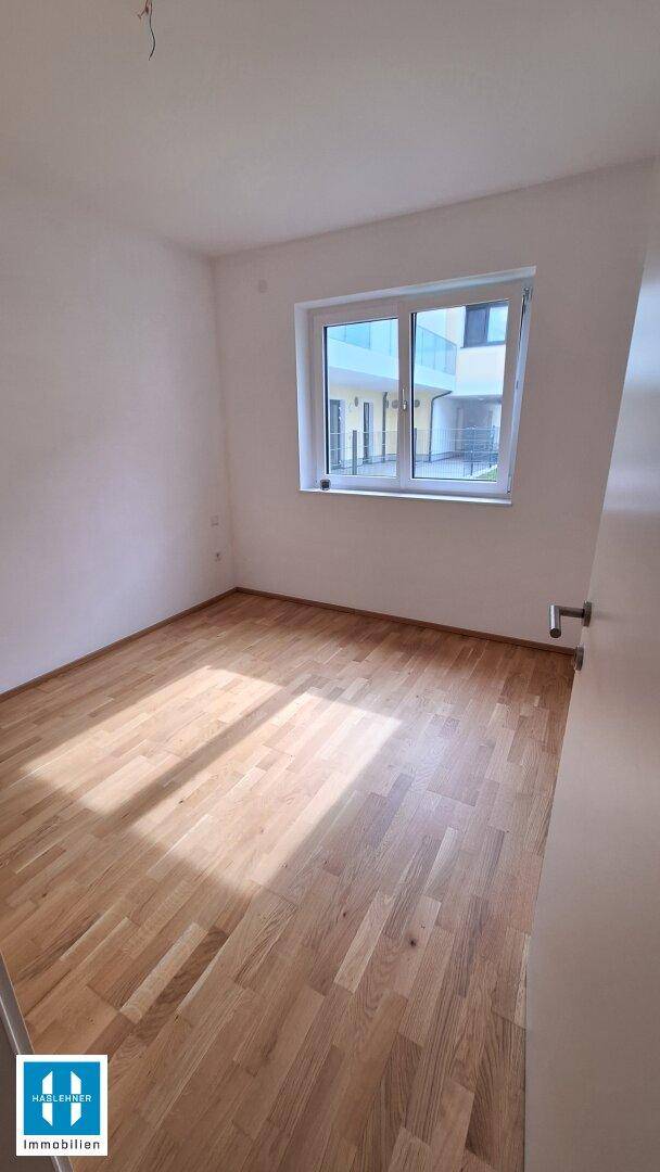 Helles, unmöbliertes Schlafzimmer mit Holzboden und Fenster, das viel Licht hereinlässt.