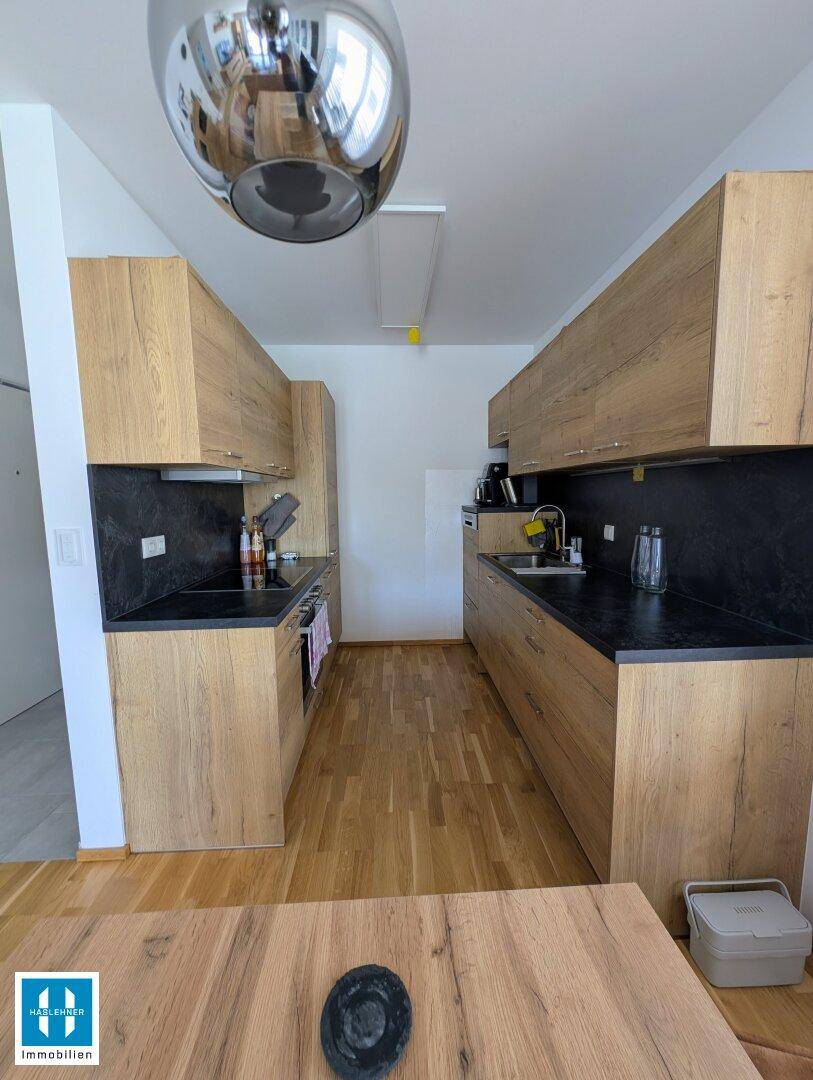 Funktionale Küche mit Holzschränken, dunklen Arbeitsplatten und integrierten Geräten.