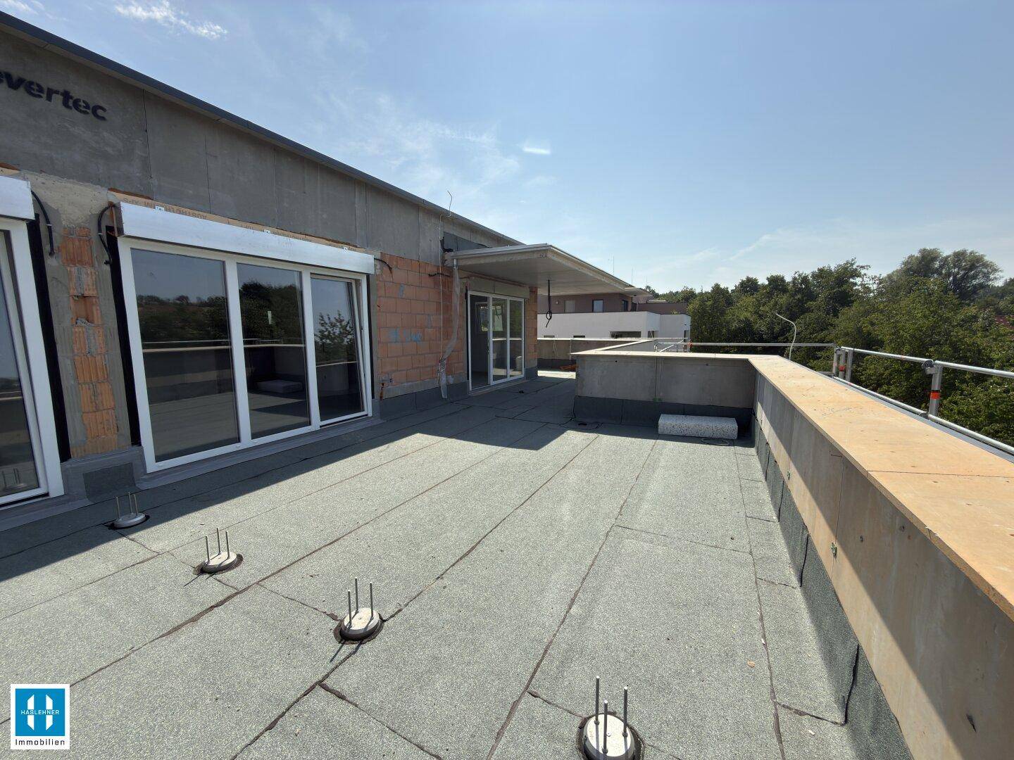 Große, unfertige Dachterrasse mit Blick auf die Umgebung und sichtbaren Baumaterialien.
