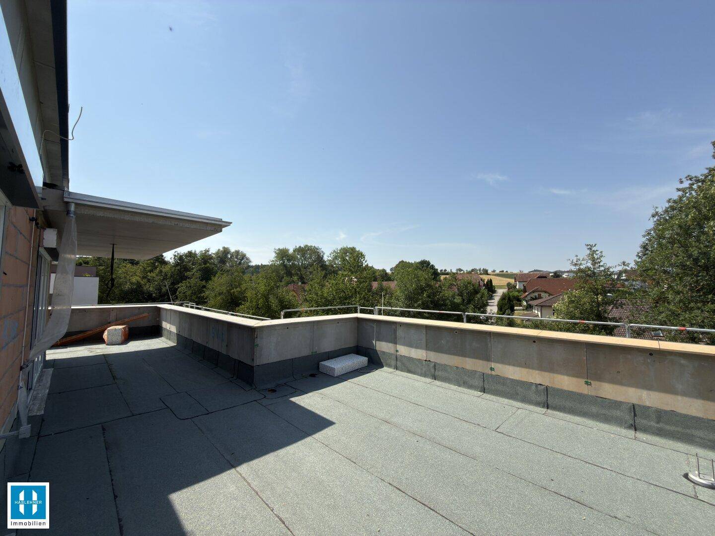 Weitläufige Dachterrasse im Rohbau mit Panoramablick über die grüne Landschaft und den Horizont.