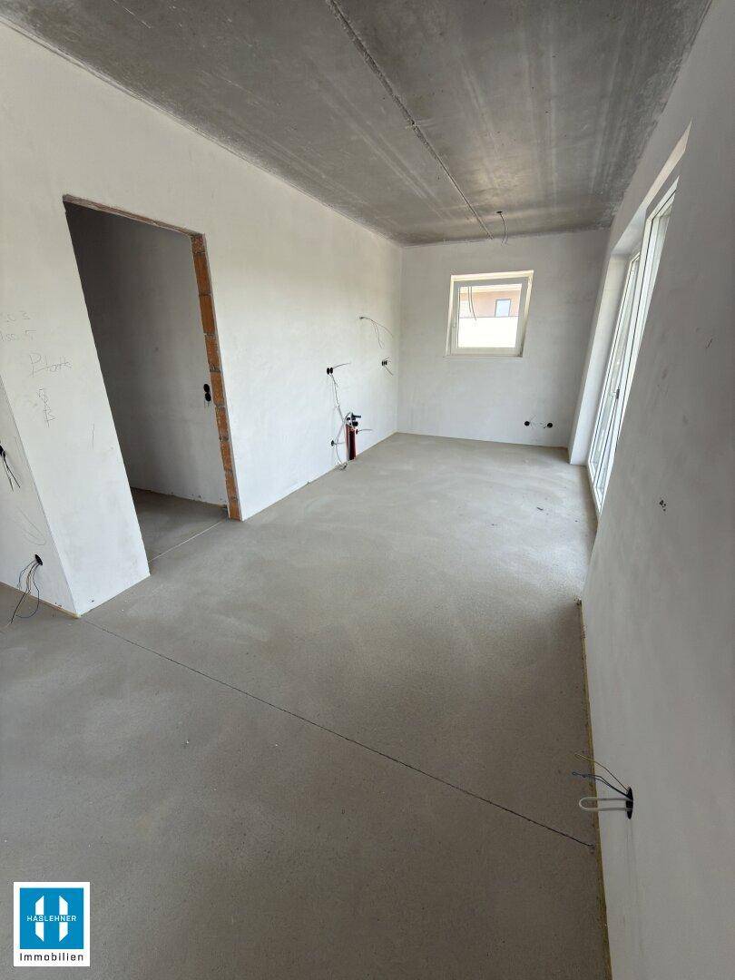 Unfertiger Raum mit Betonboden, einem Fenster und sichtbaren Elektroinstallationen an den Wänden.