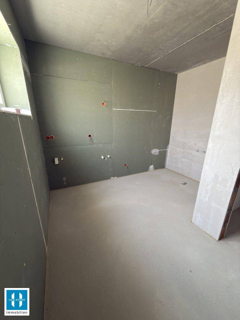 Unfertiger Raum mit feuchtigkeitsbeständigen Wänden, Betonboden und sichtbaren Sanitäranschlüssen.