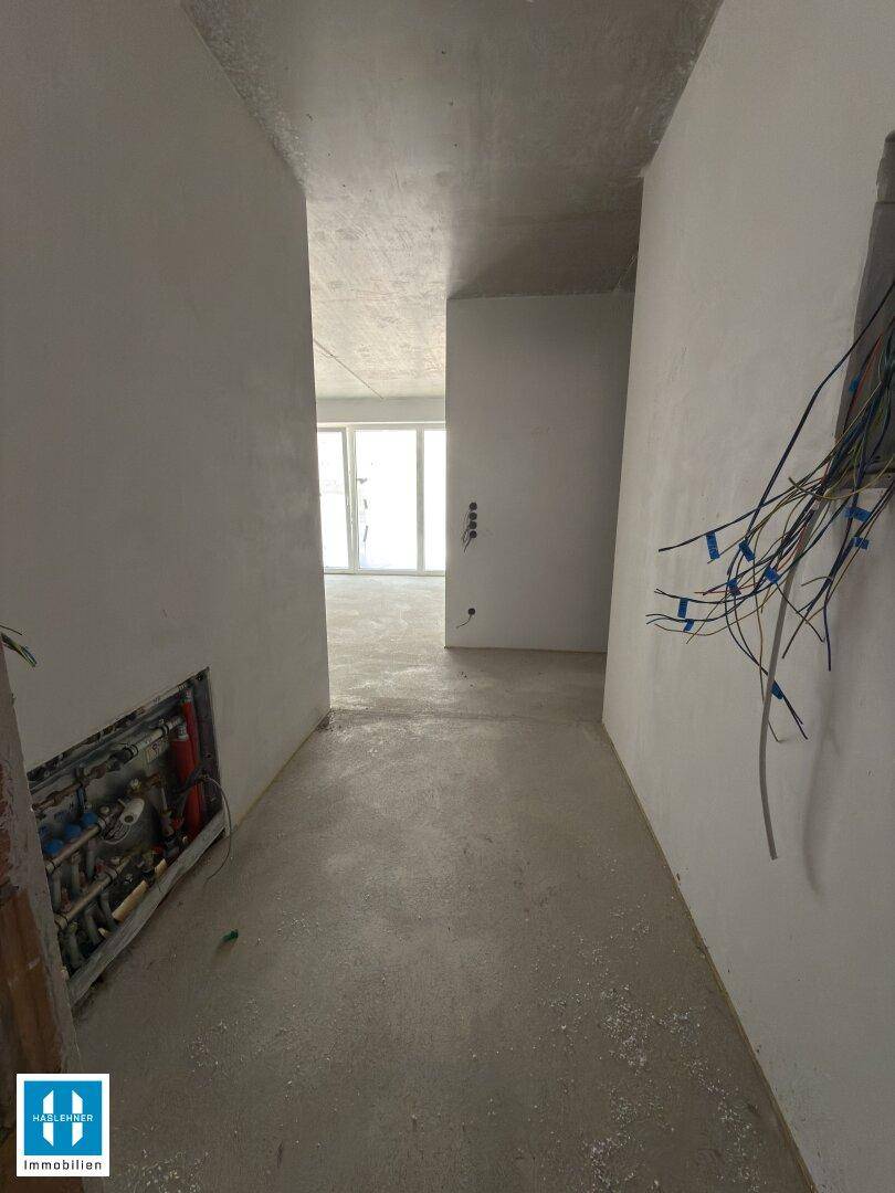Unfertiger Flur mit sichtbaren Installationen und Blick in einen hellen, zukünftigen Wohnbereich.