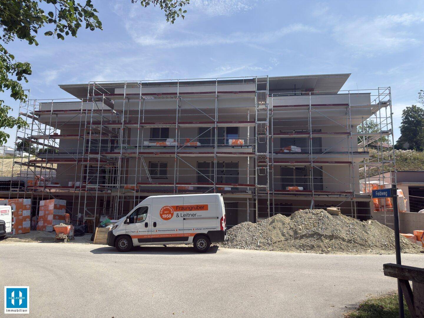 Neubaugebäude im Rohbauzustand mit Gerüst und Lieferwagen auf der Baustelle.