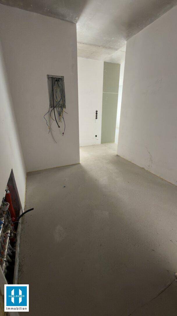 Unfertiger Innenraum mit sichtbaren Installationen und Betonboden, wartet auf den weiteren Ausbau.