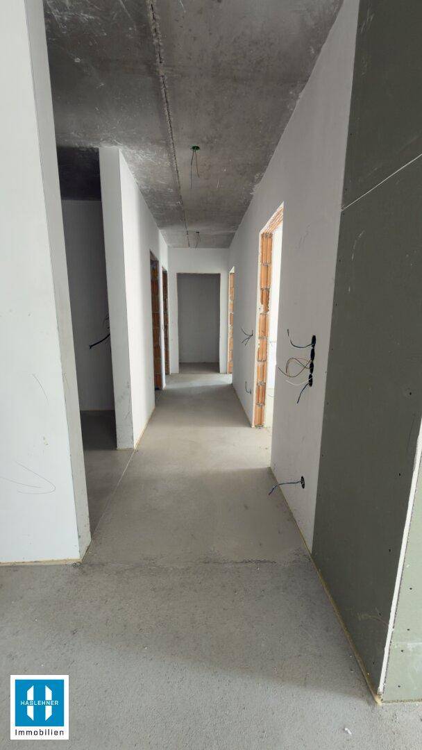Langer Flur im Rohbauzustand mit Betonboden und unverputzten Wänden, bereit für den Innenausbau.