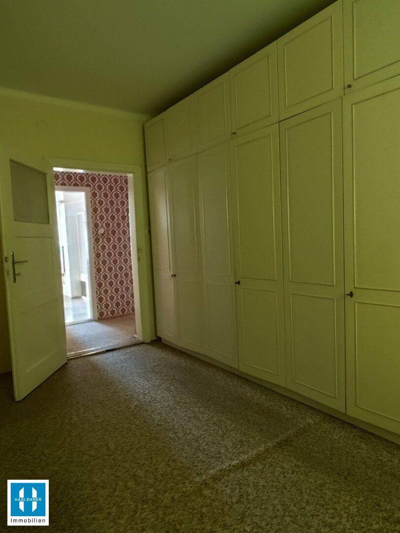 Schlafzimmer mit großem Einbauschrank und Teppichboden, angrenzend an einen weiteren Raum.