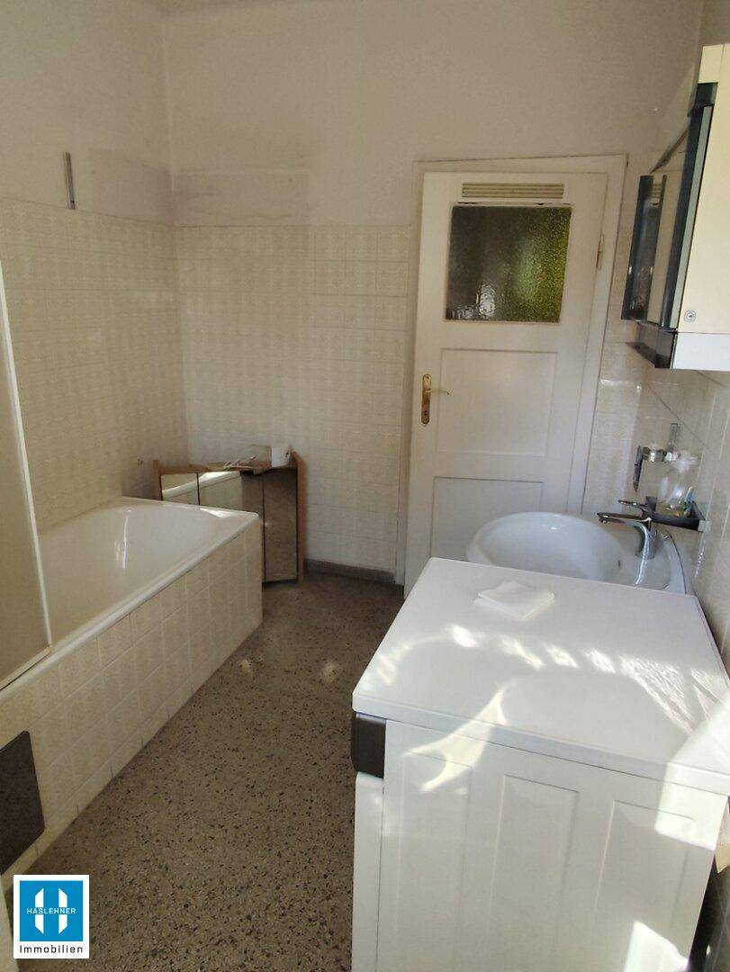 Badezimmer mit Badewanne, Waschbecken und Waschmaschine, gefliesten Wänden und Boden.