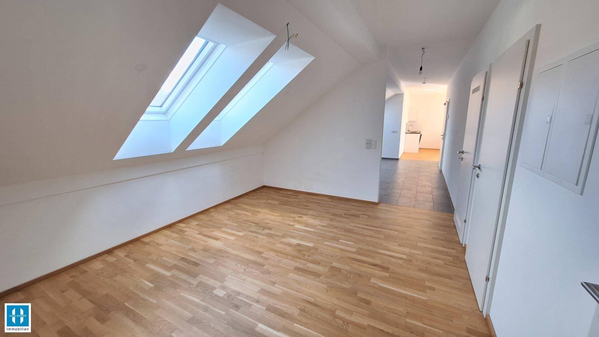 Geräumiges Zimmer im Dachgeschoss mit Holzboden und zwei großen Dachfenstern für viel Licht.