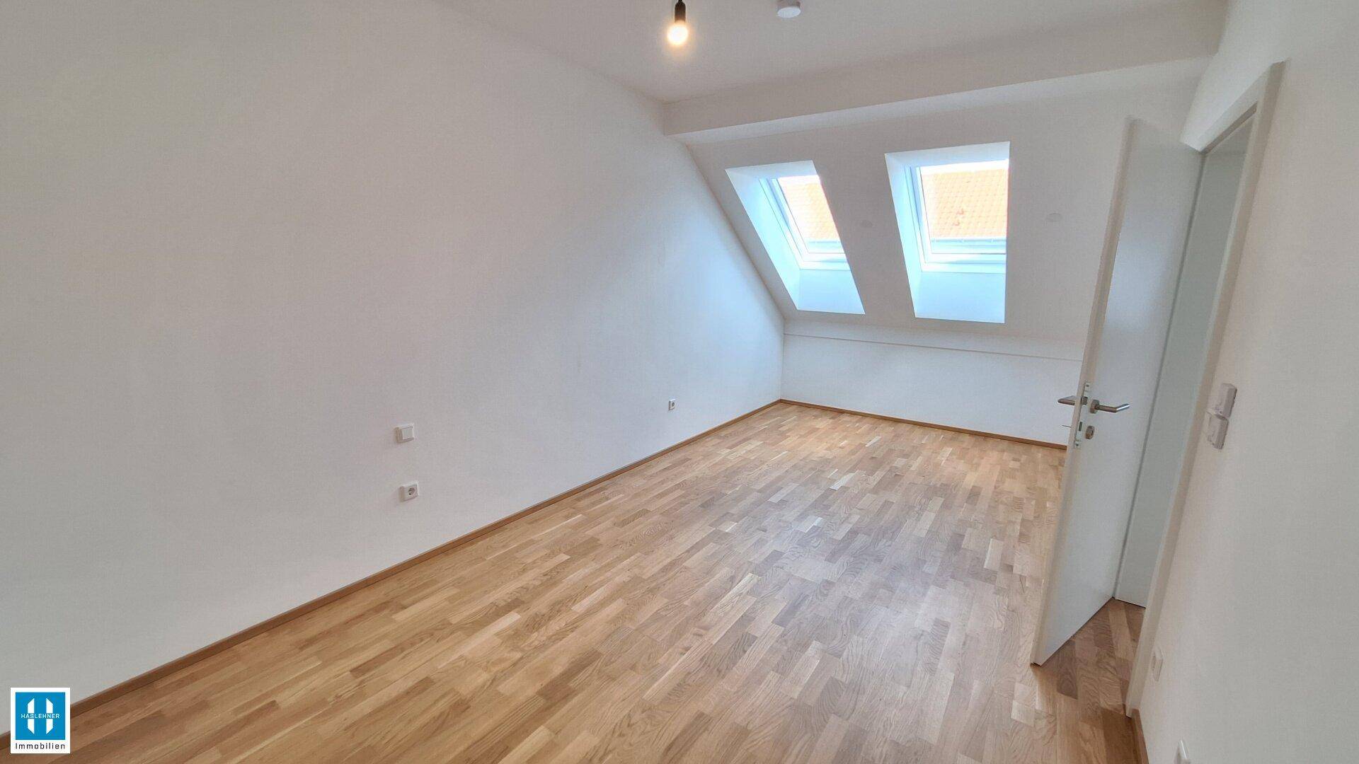 Helles Dachzimmer mit Holzboden und schrägen Wänden, ideal als Schlaf- oder Arbeitszimmer.