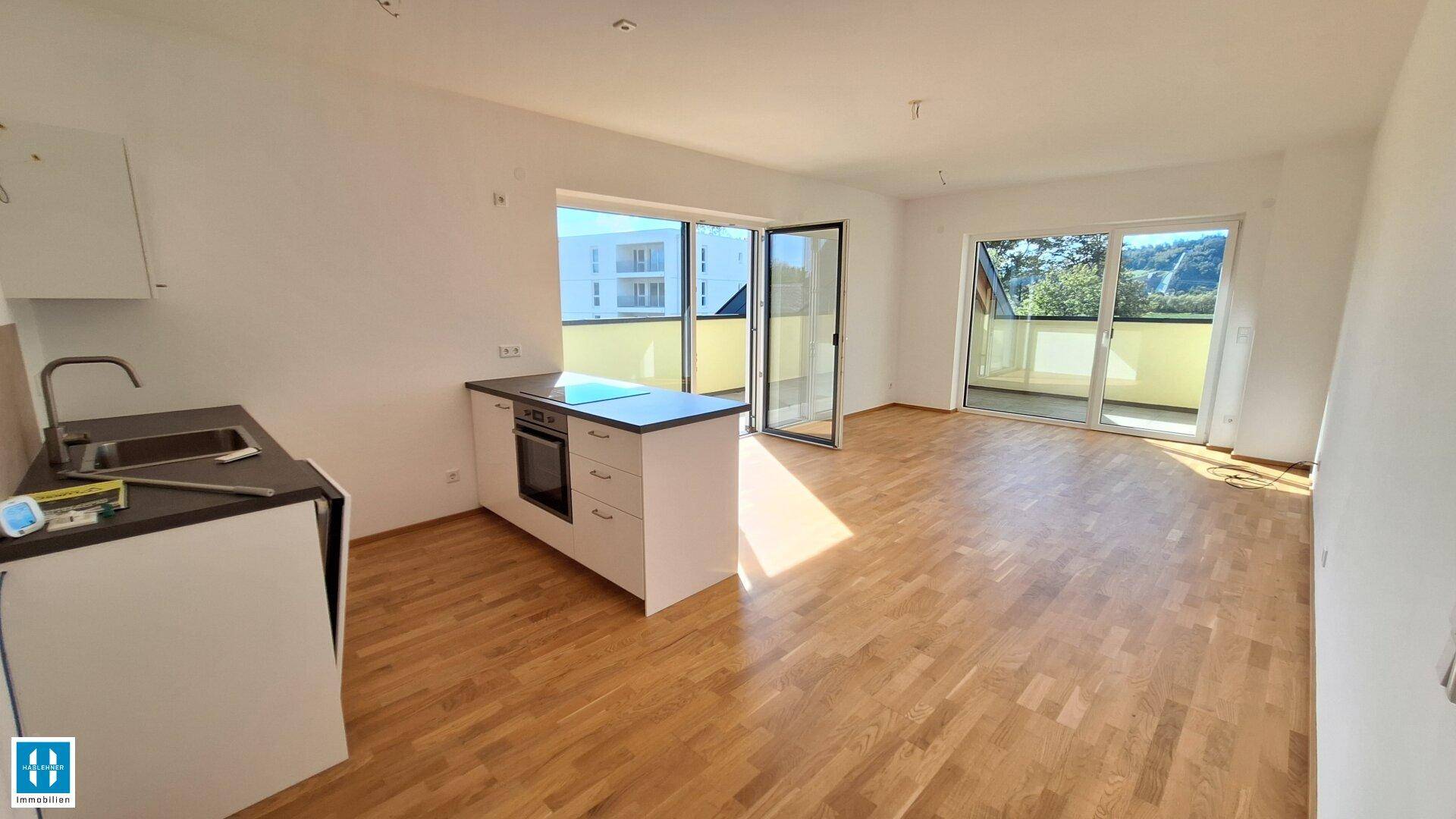 Heller offener Wohnbereich mit Holzboden, Küchenzeile und Zugang zu einem sonnigen Balkon.