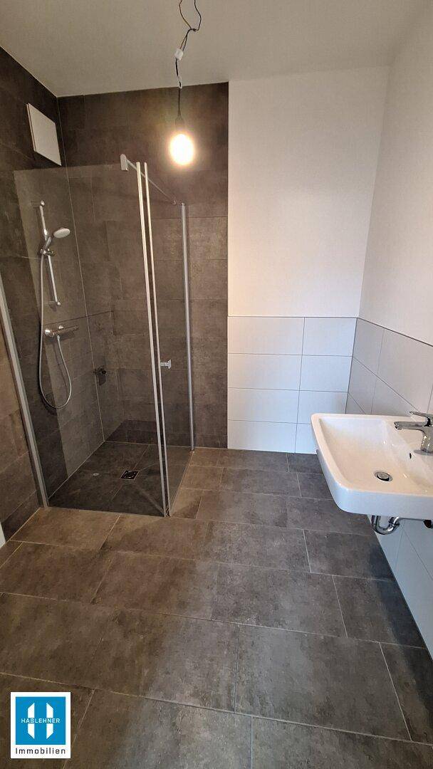 Modernes Badezimmer mit begehbarer Dusche, dunklen Fliesen und einem einzelnen Waschbecken.