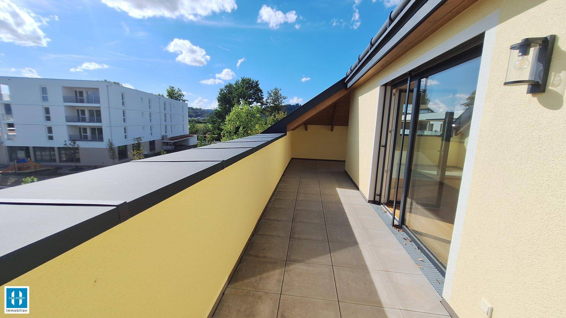 Heller Terrassenbereich mit Fliesenboden und Zugang zu den Innenräumen, umgeben von Natur.