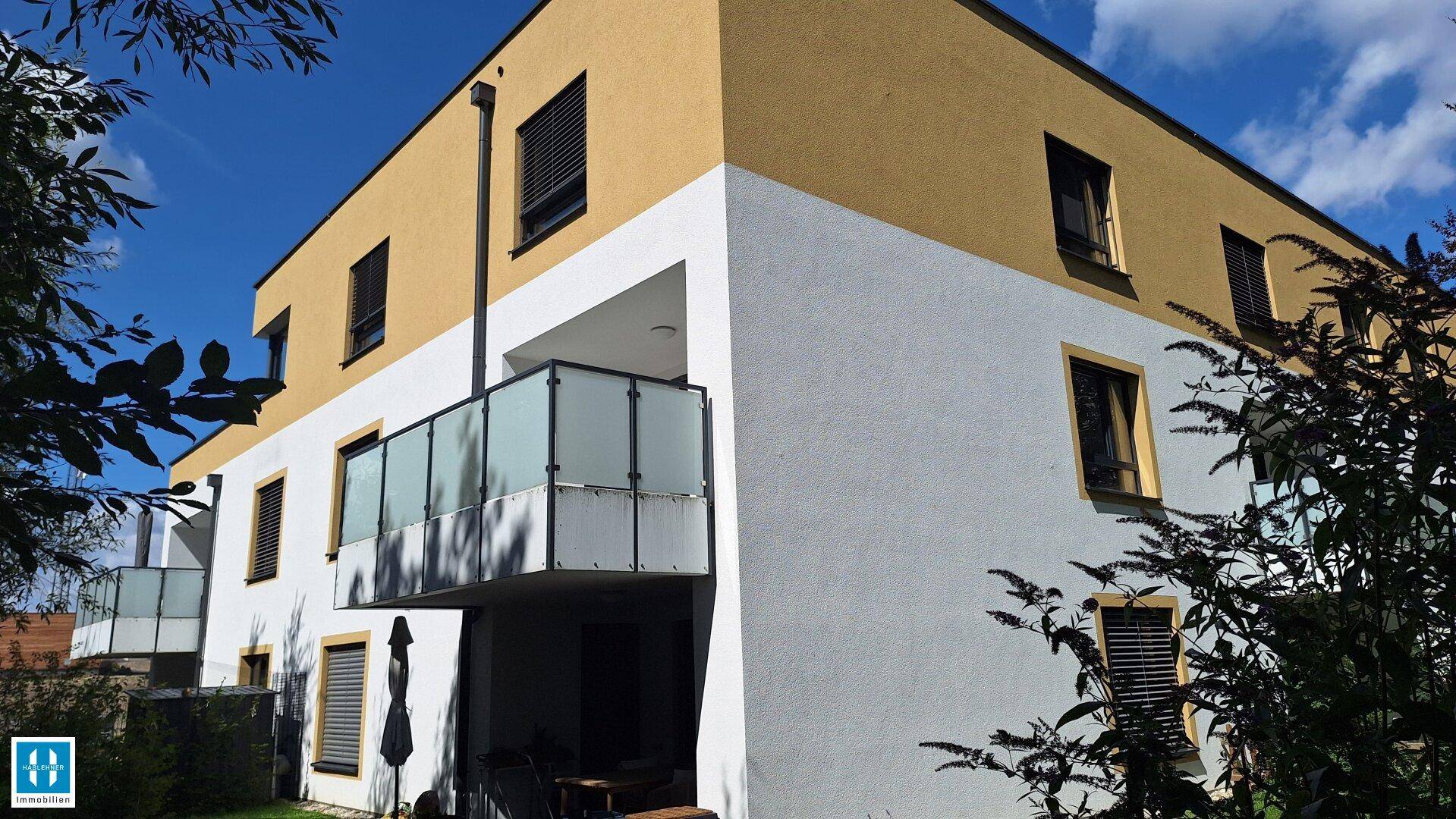 Moderne Wohnanlage mit gelb-weißer Fassade und Balkonen in grüner Umgebung.