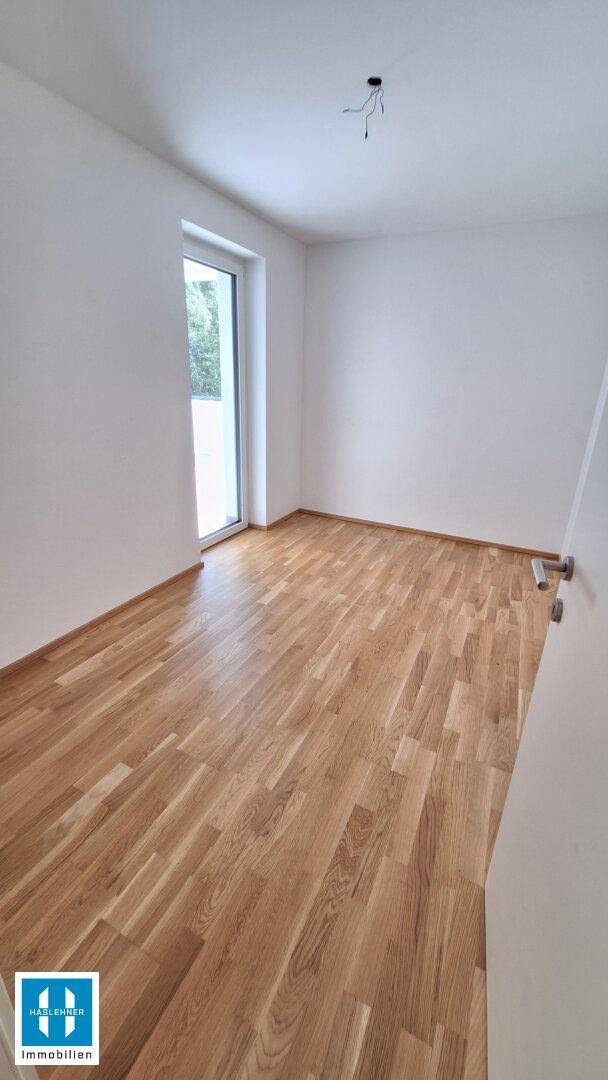 Helles Zimmer mit Parkettboden und großem Fenster, ideal als Schlaf- oder Arbeitszimmer.