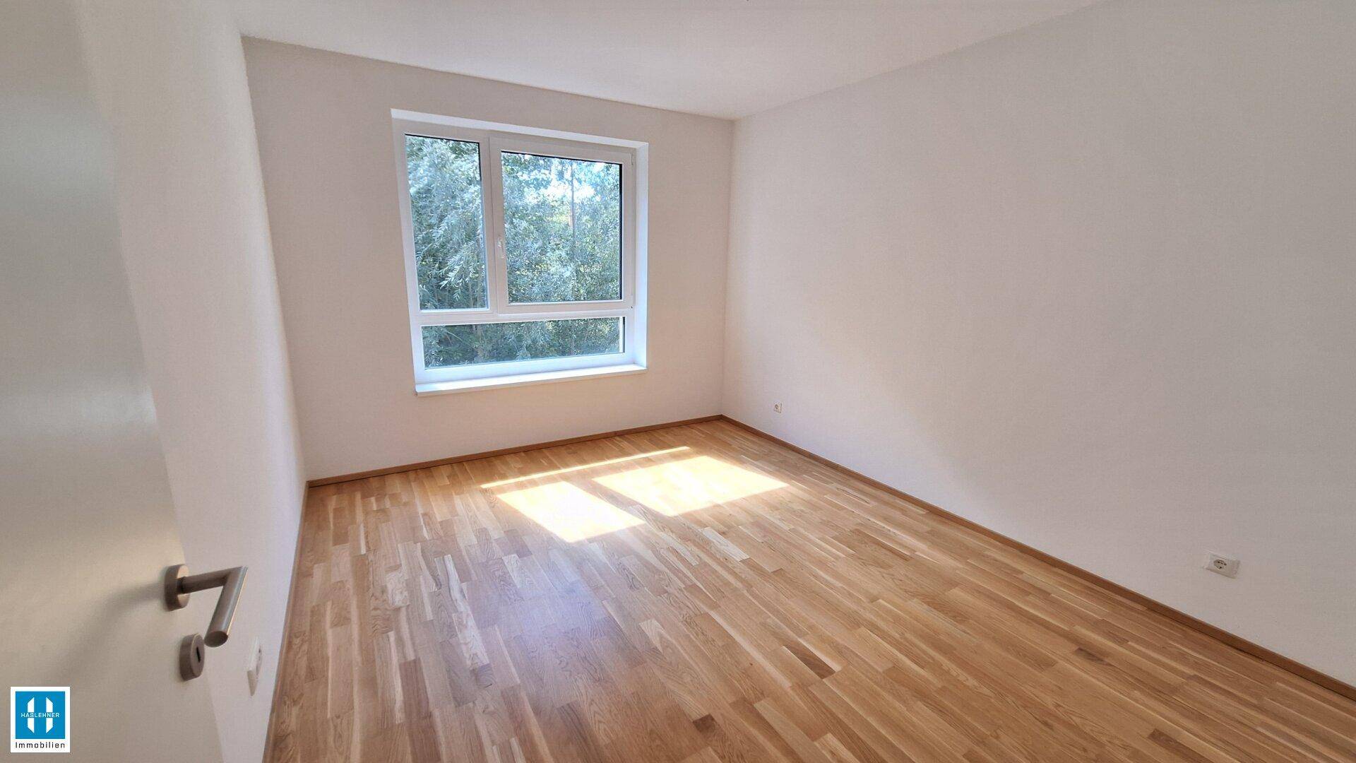 Geräumiges Zimmer mit Parkettboden und viel Tageslicht durch das große Fenster.