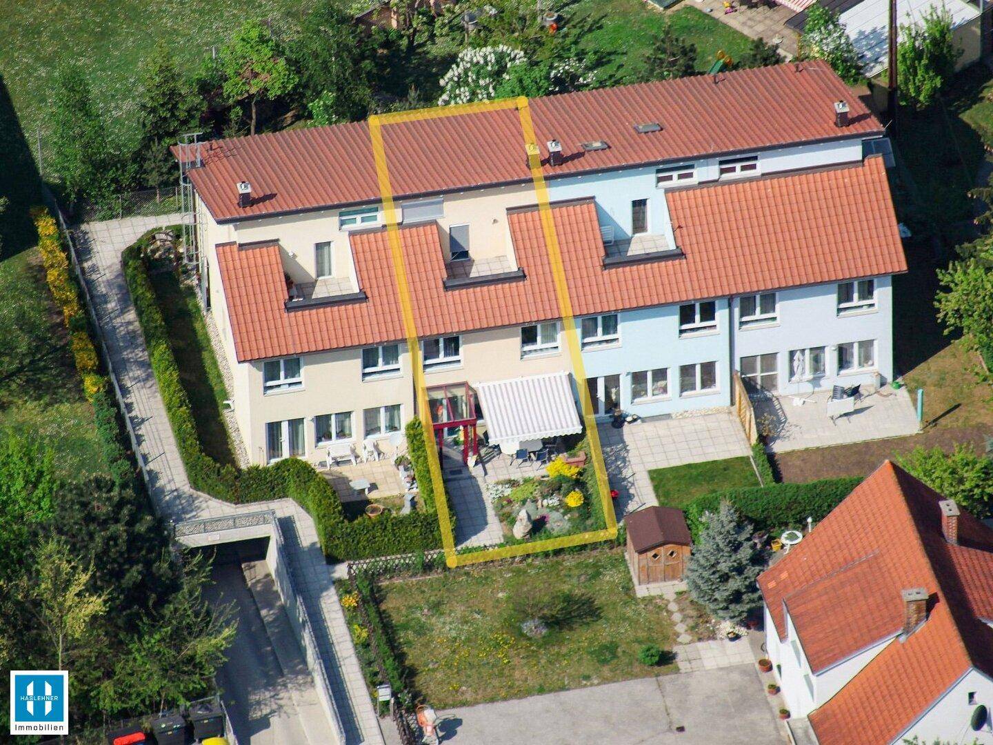 Luftaufnahme eines Reihenhauskomplexes mit Gärten und Terrassen, umgeben von viel Grün.