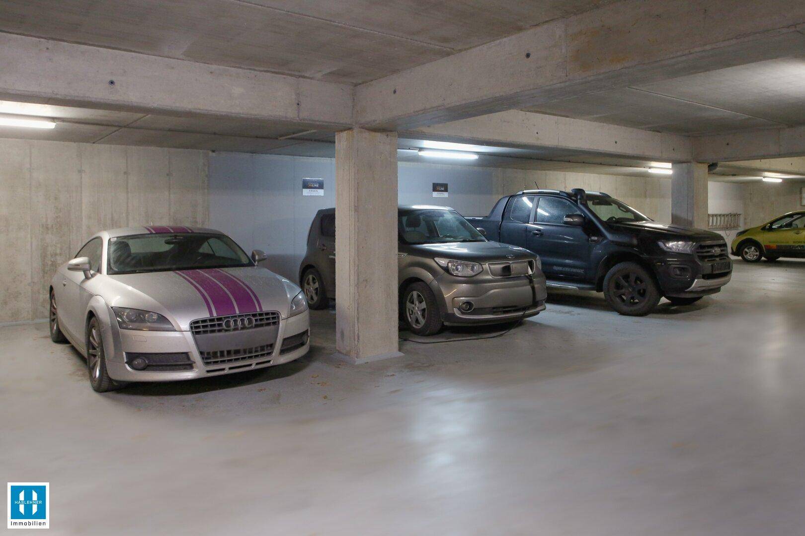 Geräumige Tiefgarage mit mehreren geparkten Fahrzeugen und Betonwänden.