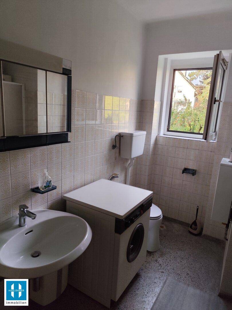 Funktionales Badezimmer mit Toilette, Waschbecken und Fenster, hell gefliest und mit Spiegelschrank.
